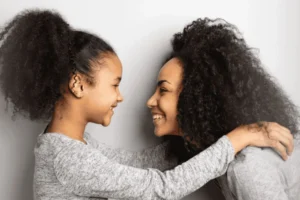 Smiling mother and daughter face each other and embrace, symbolizing trust and openness in teaching anatomically correct terms.